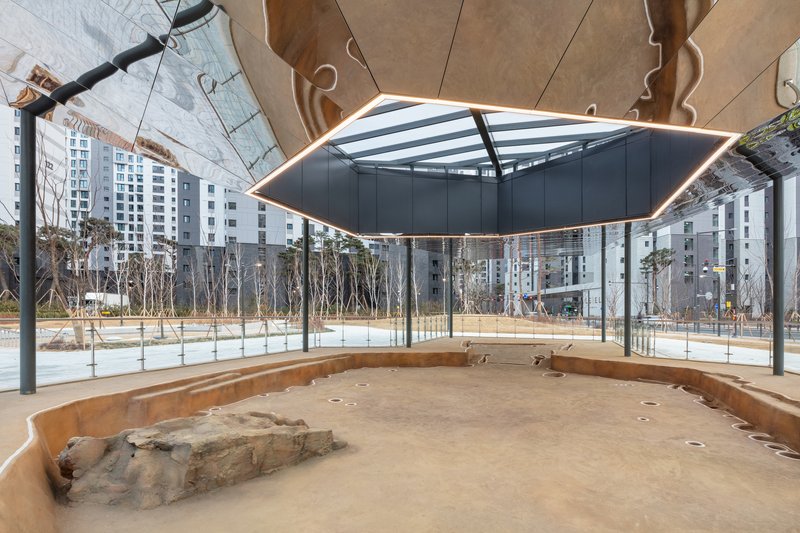 Interior view beneath the canopy showing exposed rock formations on the sand floor and glass perimeter walls