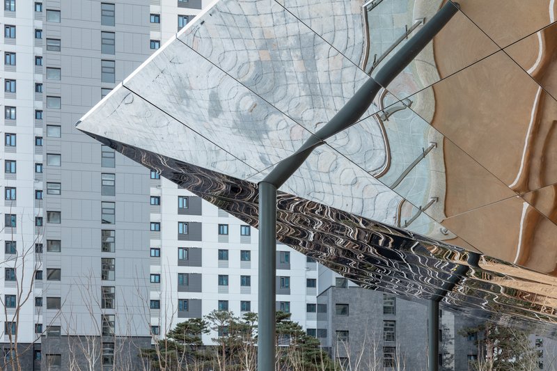 Underside detail of the reflective stainless steel and textured copper roof panels meeting at a beam