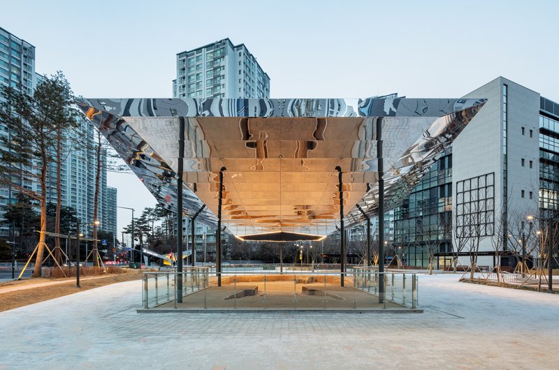 Frontal view of the mirrored underside canopy hovering above the glazed enclosure in early evening light