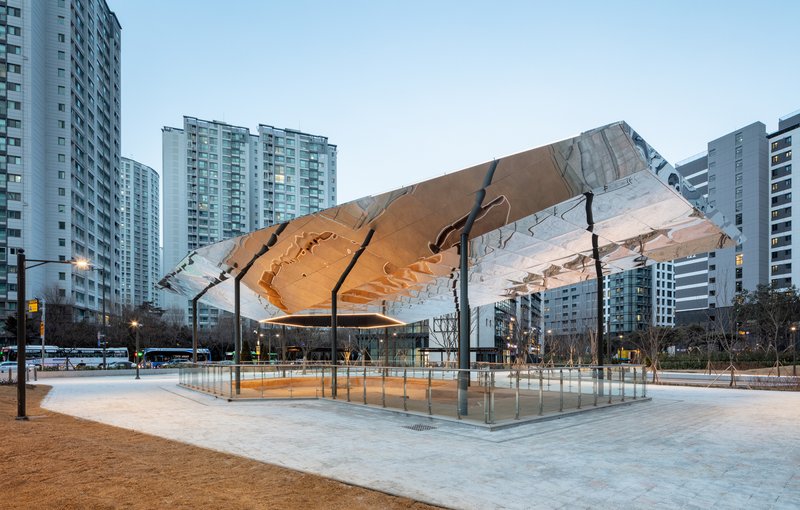 Angled view of the folded timber canopy structure framed by residential towers at twilight
