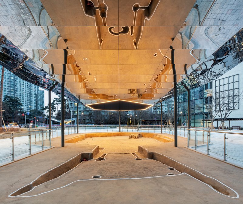 Upward view showing timber panels with irregular apertures and reflective surfaces above the circular plaza