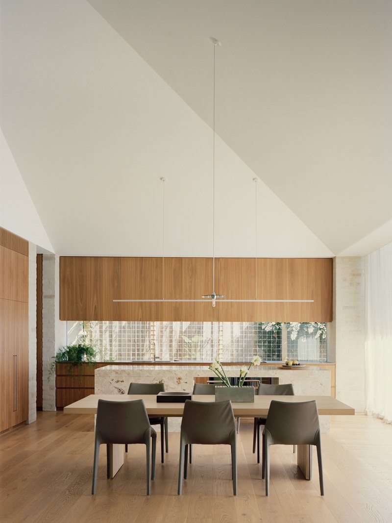 Dining area beneath vaulted ceiling with timber cabinetry and mosaic tile backsplash in soft daylight