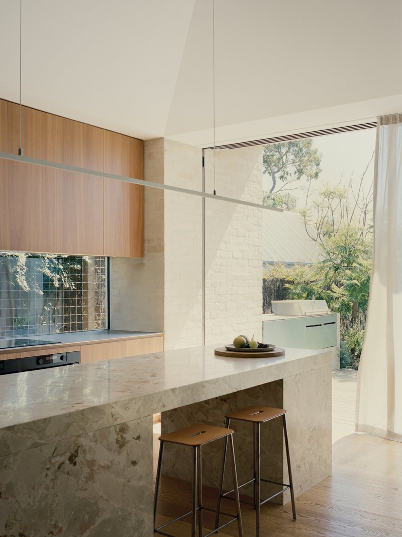 Kitchen island in mottled stone with timber cabinetry and glass doors opening to courtyard