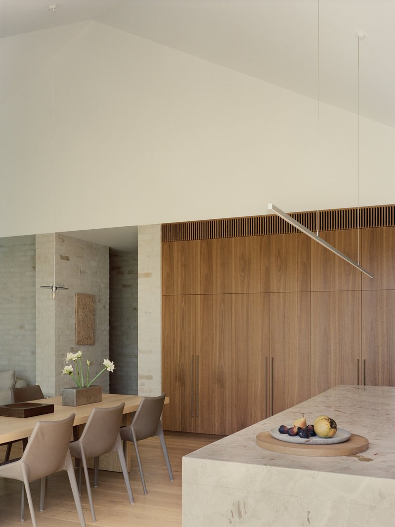Open dining area with timber storage wall and suspended linear pendant above stone island