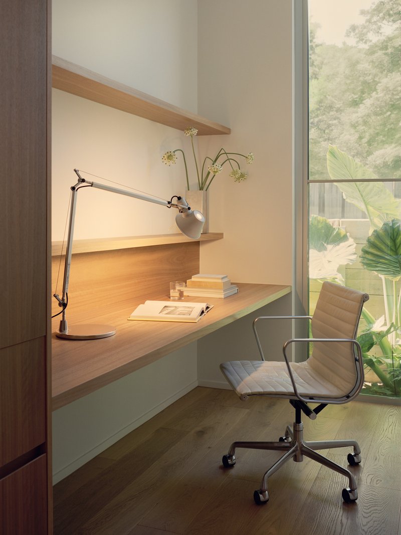 Built-in timber desk with task lamp beside a full-height window overlooking tropical planting