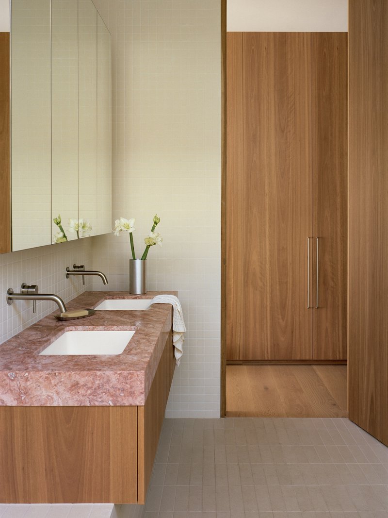 Double vanity with pink stone countertop and white tile backsplash adjacent to timber wardrobe doors
