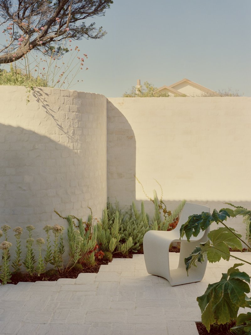 Terraced courtyard with curved stucco walls, planted beds of grasses and cacti, and a white sculptural seat