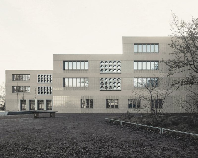 Stepped facade with alternating rectangular windows and circular perforated panels in pale brick under an overcast sky