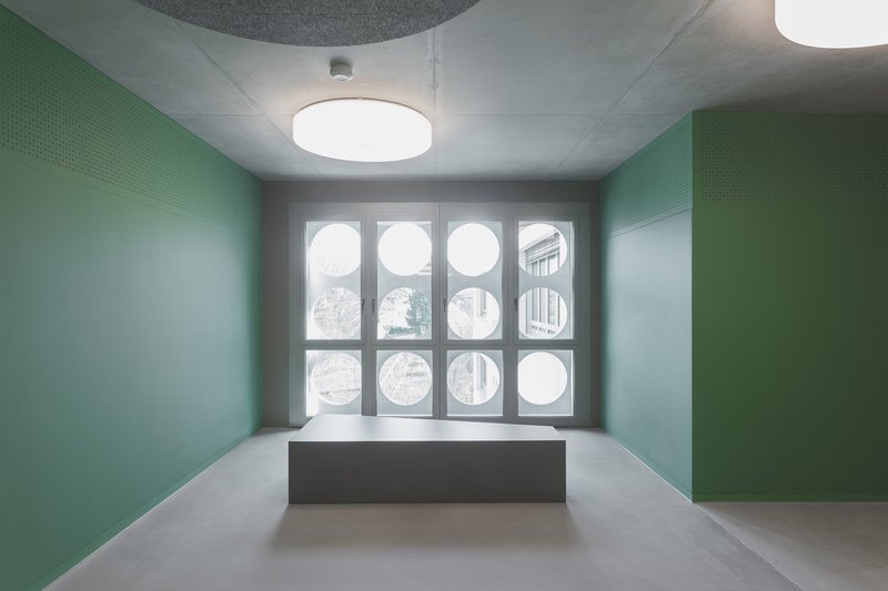 Interior room with green perforated wall panels and grid of circular windows beneath drum pendant lights