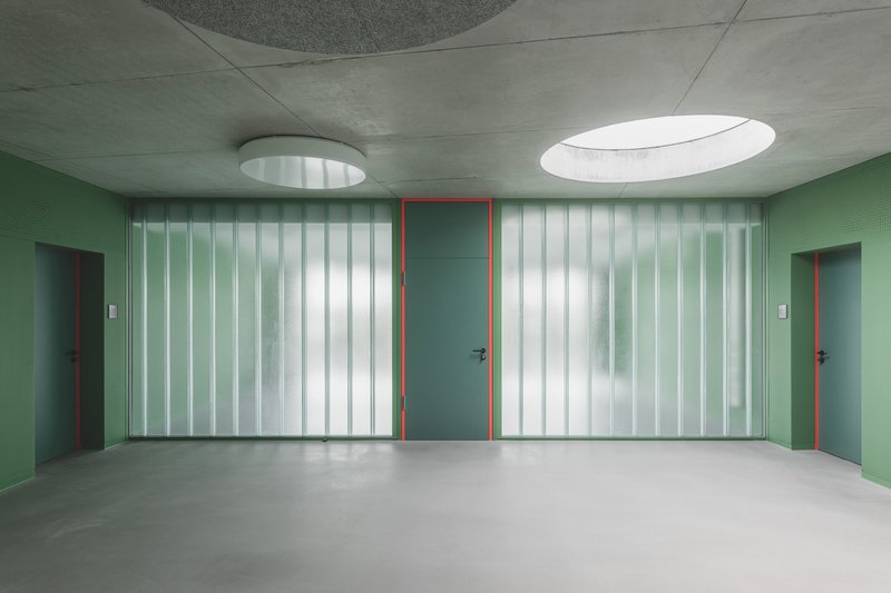 Corridor with translucent vertical glass panels flanking doors painted in green and red under oval skylights