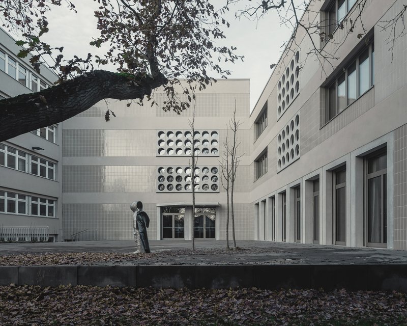 Courtyard view between buildings with a person walking beneath bare tree branches and fallen leaves