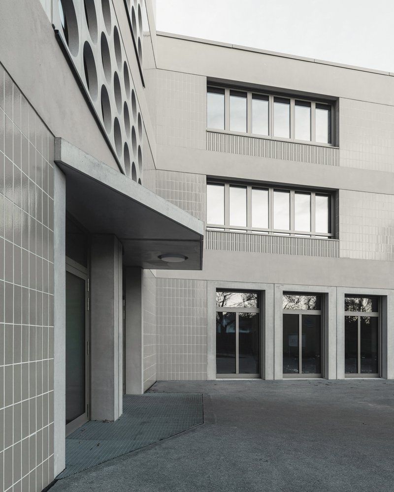 Courtyard entrance with light tile facade, recessed doorway, and horizontal ribbon windows under overcast sky