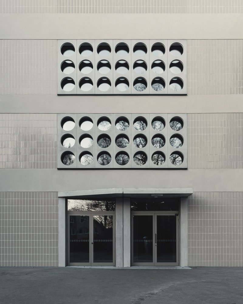 Facade detail showing two rows of circular openings with deep reveals above glazed entrance doors