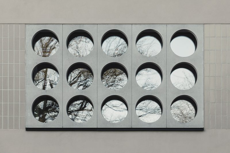 Close-up of fifteen circular openings in concrete panel framing views of bare tree branches