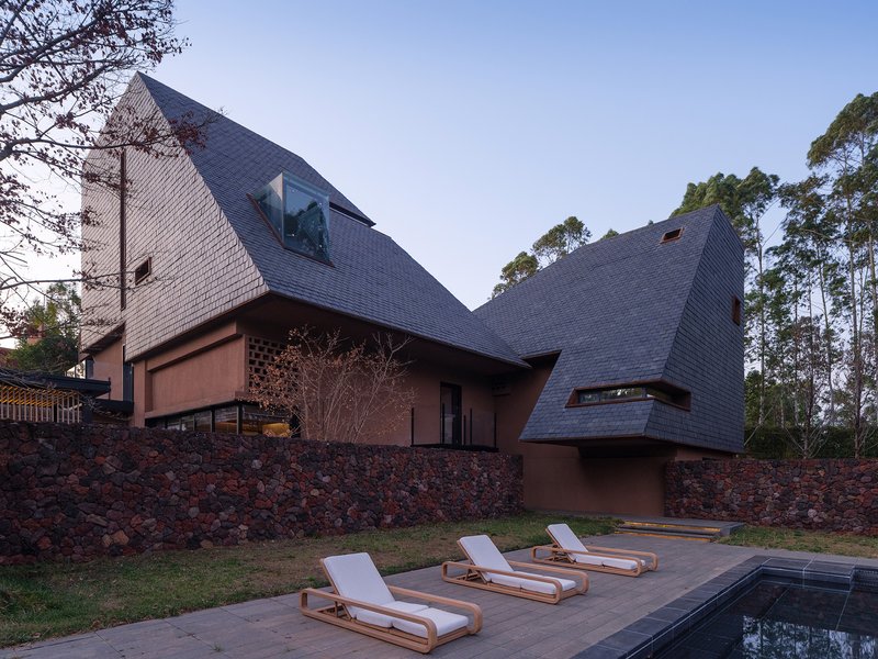 Angled dark shingle roofs overlooking a pool terrace with three white loungers at dusk
