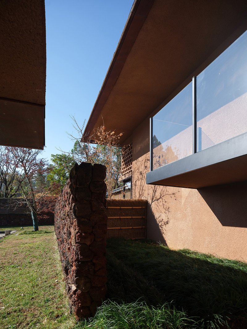 Cantilevered terrace soffit and red volcanic stone wall beneath glass balustrade in morning light