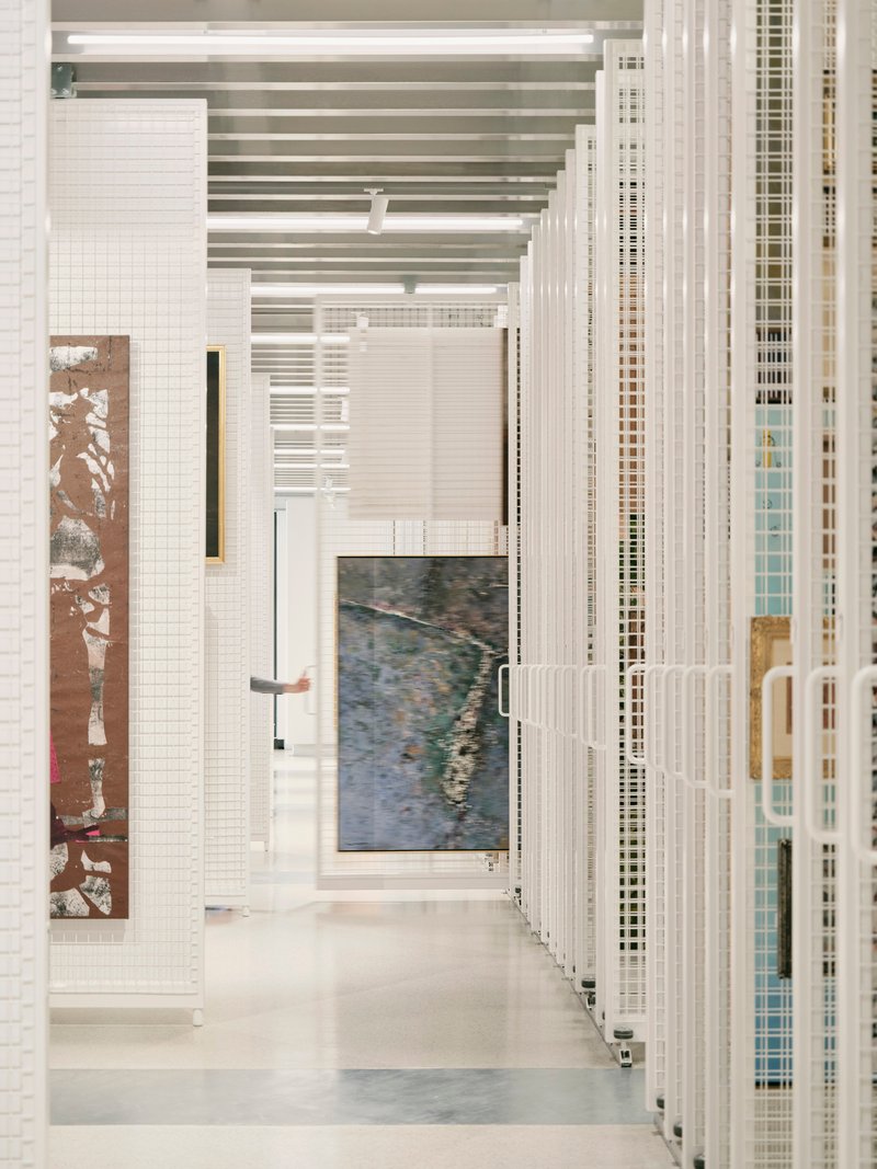 Gallery corridor with white tile walls and suspended metal grille screens beside polished concrete floors