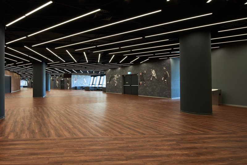 Interior lobby space with herringbone wood flooring and linear ceiling lights over dark columns and walls