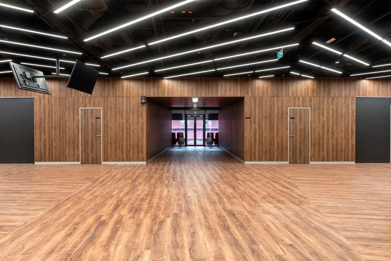 Corridor with timber paneled walls and wood flooring leading to glazed entrance doors under linear lighting