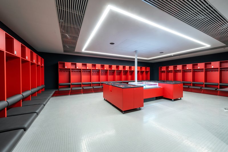 Locker room interior with red cubbies, black benches, central island units, and recessed ceiling lighting