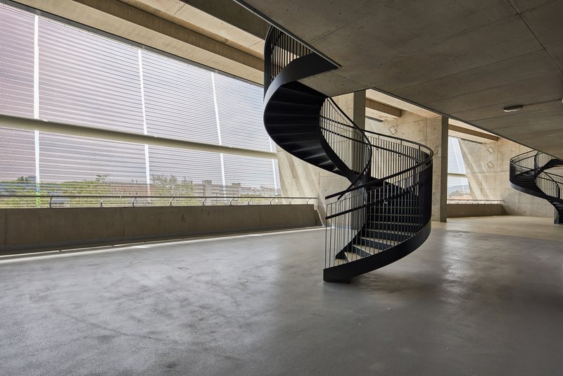 Black spiral staircase on a concrete floor with large horizontal windows overlooking a distant landscape