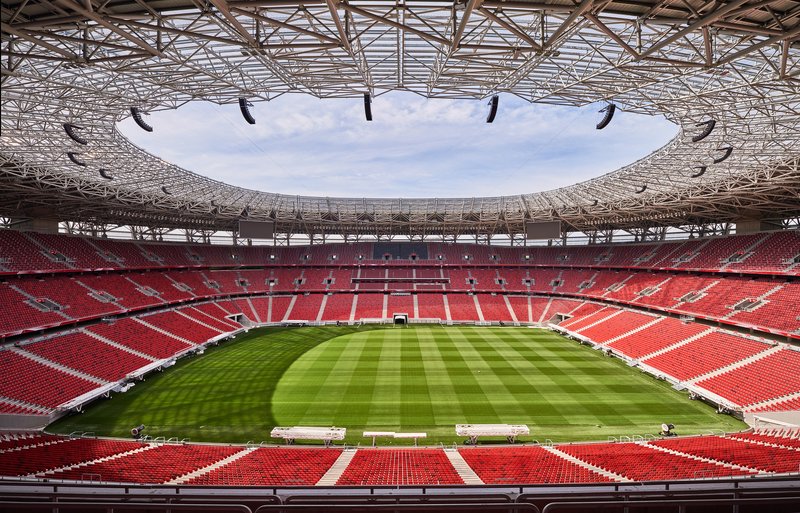 Interior view of the stadium bowl showing red seating tiers and the circular roof opening above the pitch