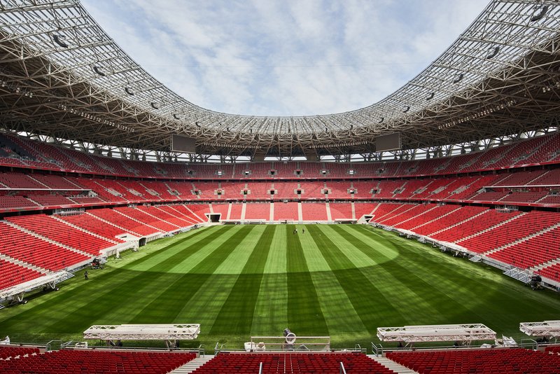 View across the stadium bowl with red seats encircling the striped pitch under the open roof