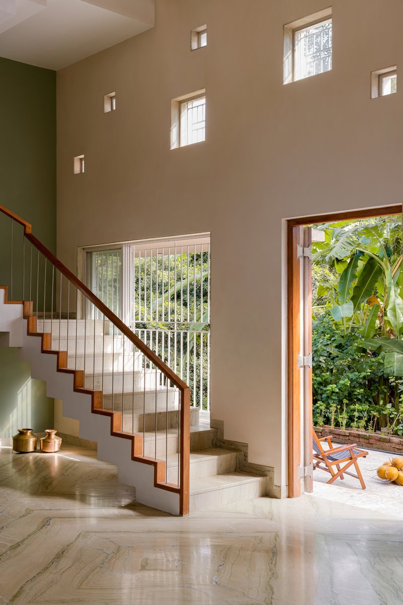Double-height stairwell with polished stone treads, vertical railings, and scattered square windows framing greenery outside