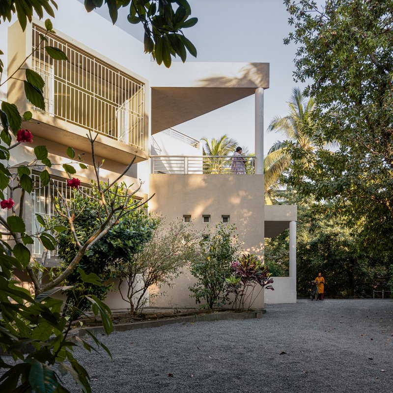 Street view of the stucco facade with planted bed and figures walking beneath overhanging palms