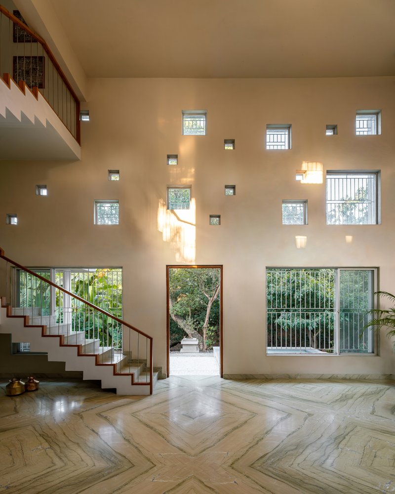 Double-height entry hall with herringbone stone floor and scattered square windows casting afternoon light