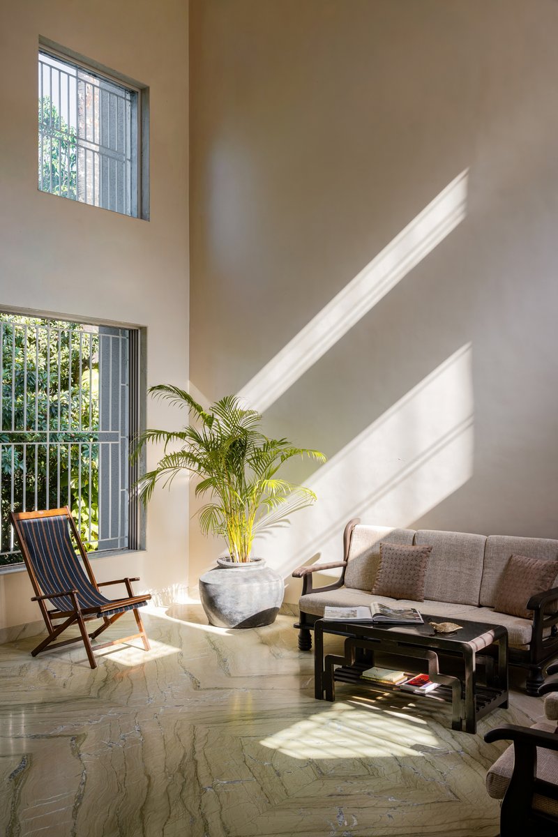 Sunlit sitting area with diagonal shadows falling across the herringbone stone floor and potted palm