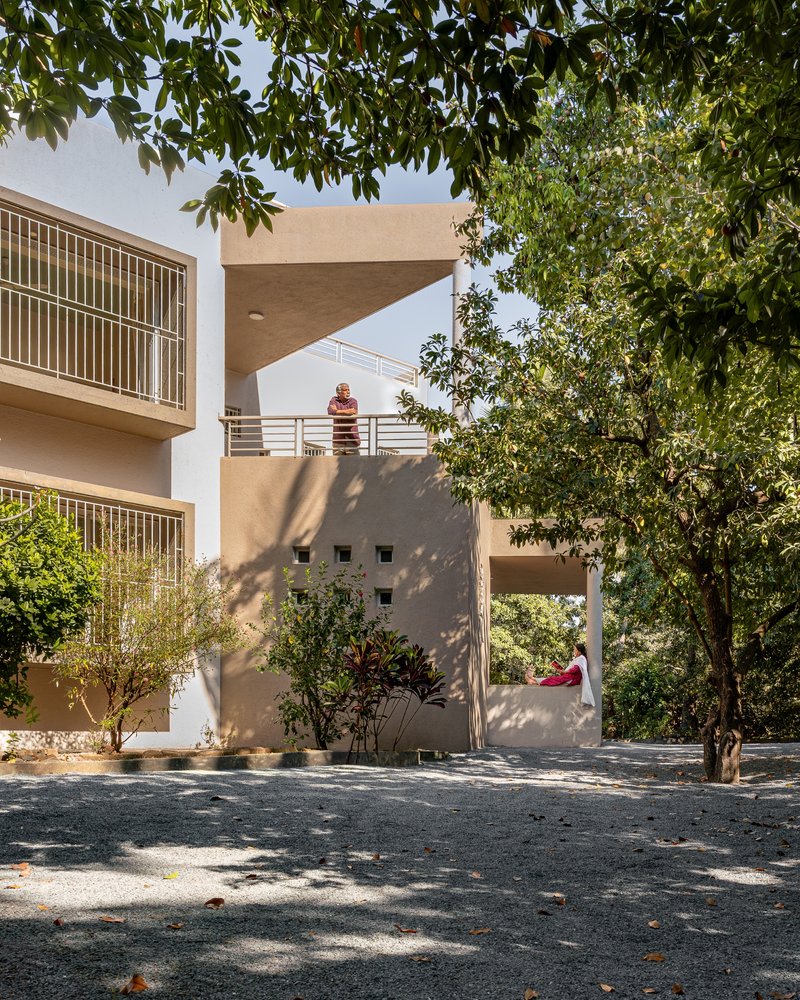 Courtyard facade with cantilevered canopy, metal railings and dappled tree shadows on gravel surface