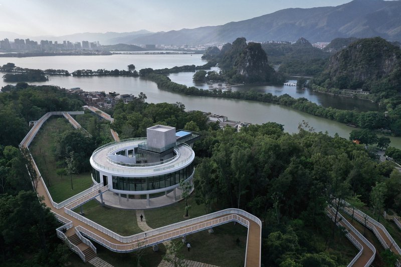 Aerial view of the circular glazed building and elevated walkways weaving through dense parkland toward a river