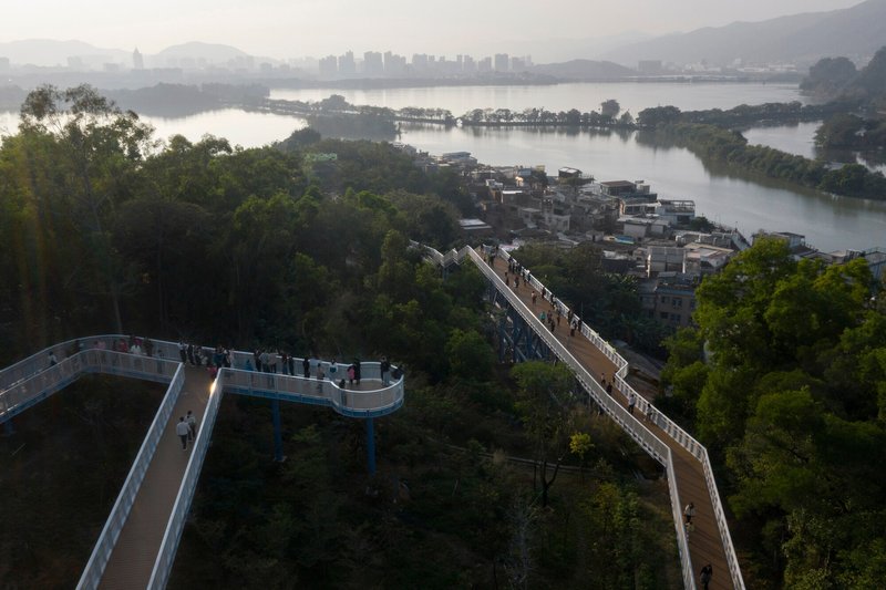 Elevated walkways zigzagging through forested parkland toward the river and distant mountains in early morning light