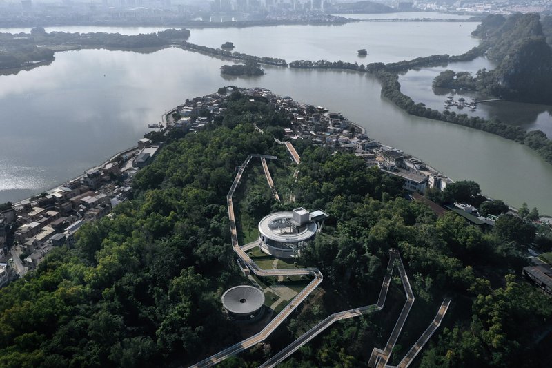 Aerial view of circular pavilions and pathways threading through forested island surrounded by lake water