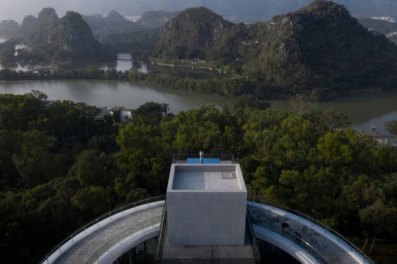 Rooftop pool terrace atop concrete volume overlooking forested valley with karst mountains and lake in morning mist