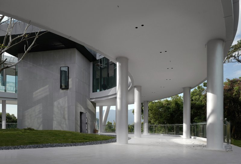 Covered terrace beneath a cantilevered floor slab supported by white cylindrical columns in afternoon light