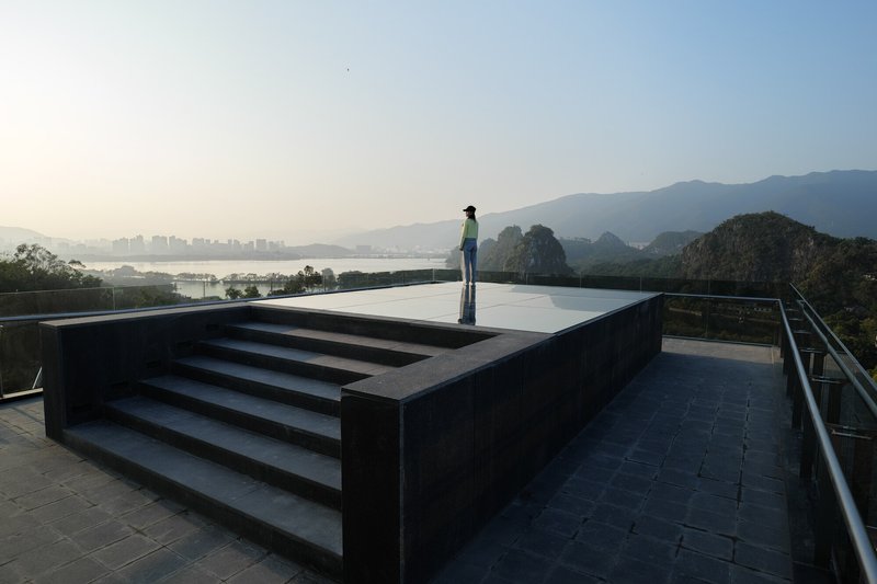 Rooftop pool with black stone surround and steps where a person stands overlooking mountains at dawn