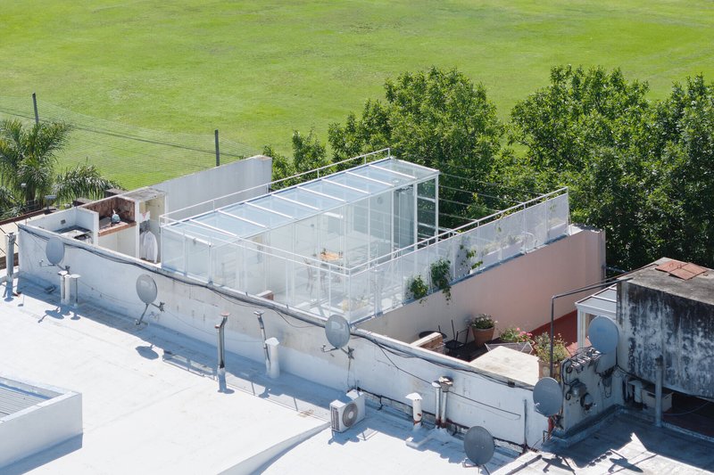 Aerial view of a glass pavilion addition atop a white-painted rooftop adjacent to surrounding green fields