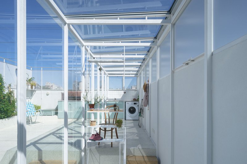 Glazed corridor with exposed white steel framing and laundry area visible inside transparent walls