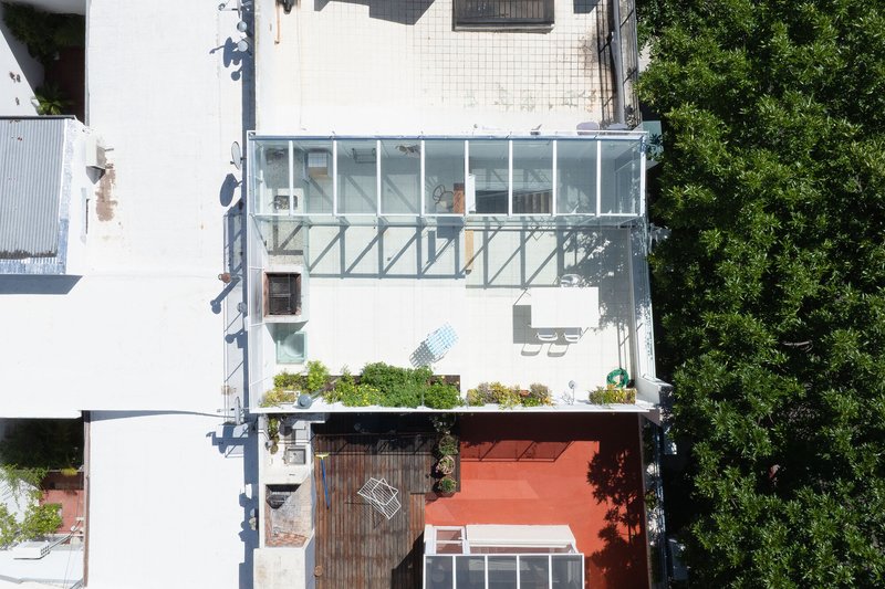 Aerial view of stacked glass volumes on a white facade with planted terrace and adjacent trees