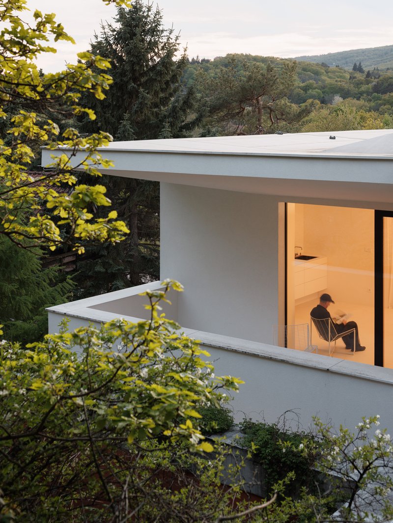 Corner terrace with flat white canopy and glazed opening where a person sits at dusk