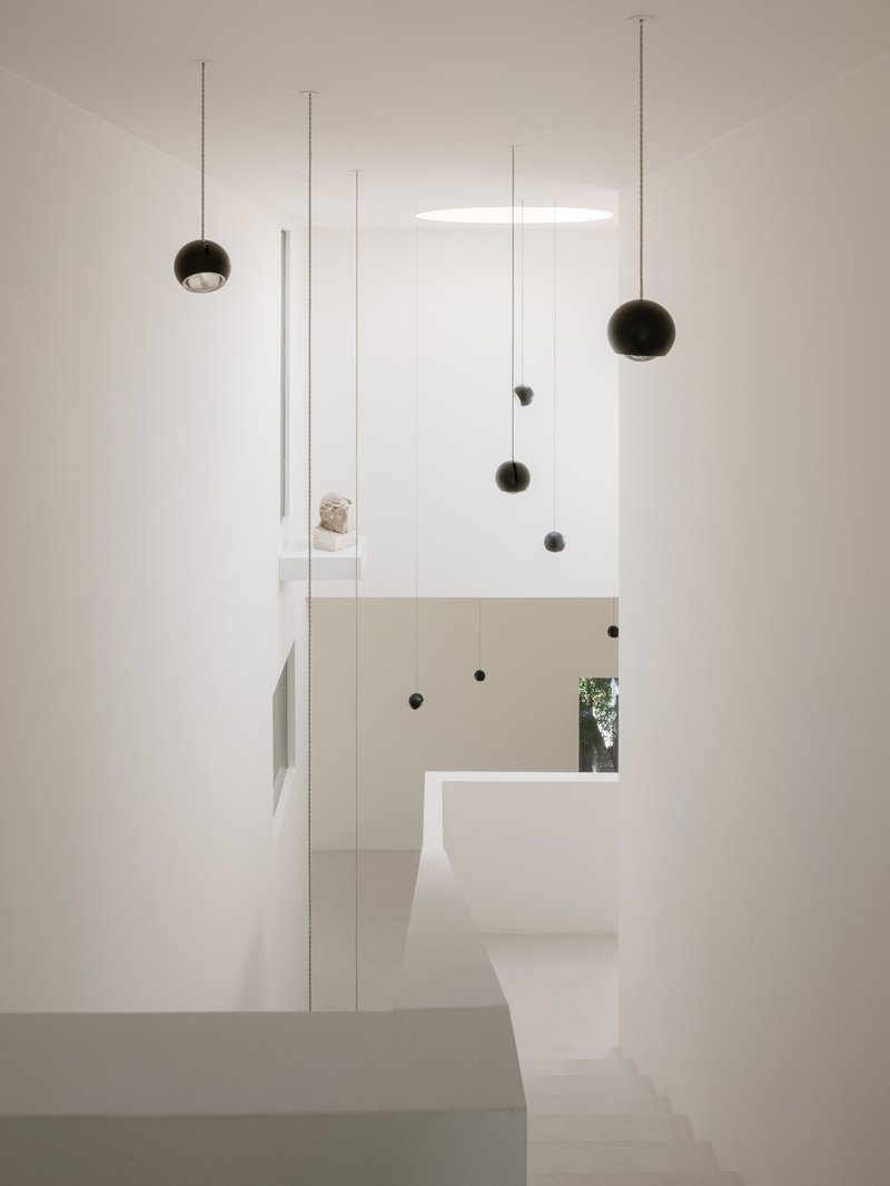 White double-height stairwell with suspended spherical pendant lights and narrow window glimpse