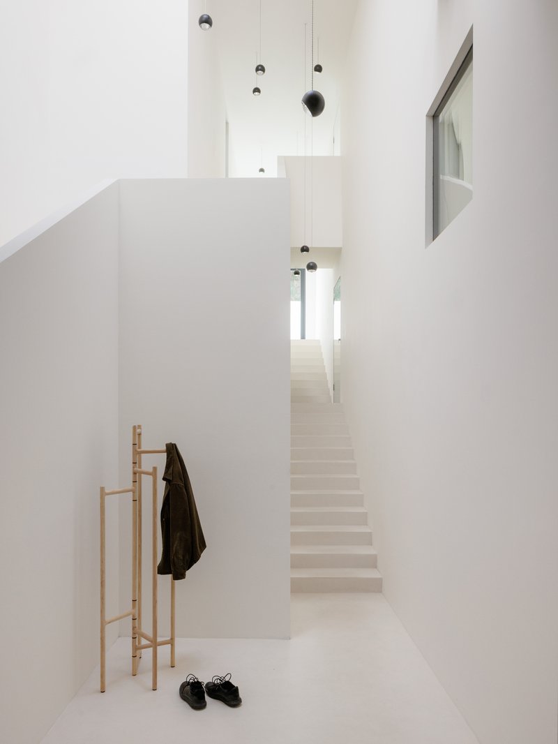 White entry hall with timber coat stand and pale staircase ascending under suspended pendant lights