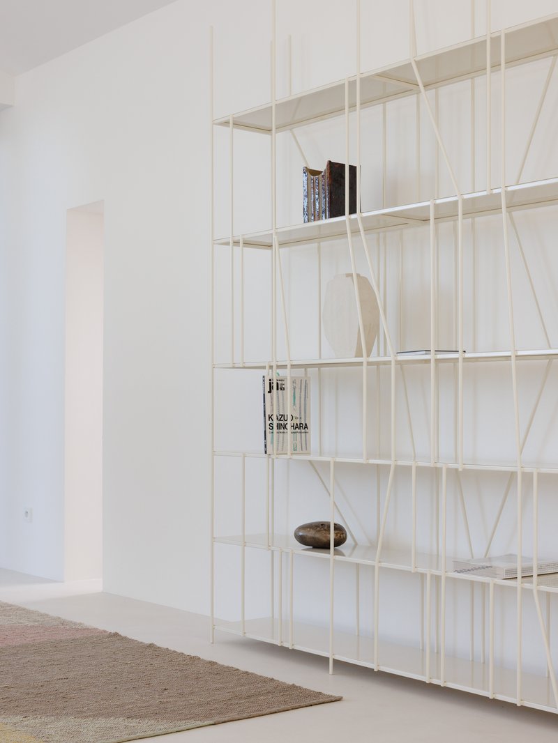 Detail of cream wire grid shelving system holding books and objects against a white wall