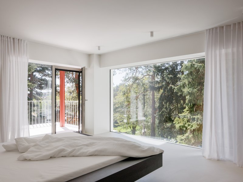 Corner bedroom windows framing treetops with sheer drapes and an open balcony door