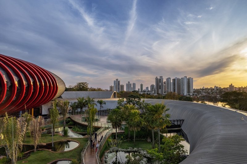 Aerial view of ribbed roofing volumes and landscaped grounds with palms against a distant skyline at sunset