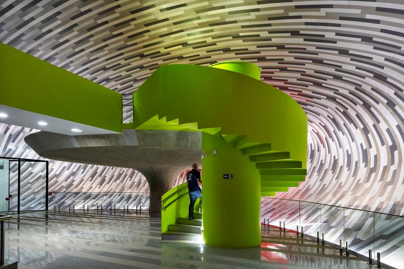 Lime green sculptural stair and foyer beneath a concentric ribbed ceiling with a visitor ascending