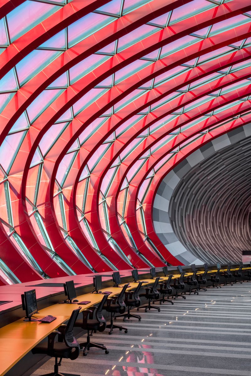 Interior workspace with curved red structural ribs and glazing panels wrapping overhead in a tunnel form