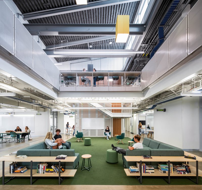 Central atrium looking up through exposed ceiling systems and balconies with students gathered on green seating